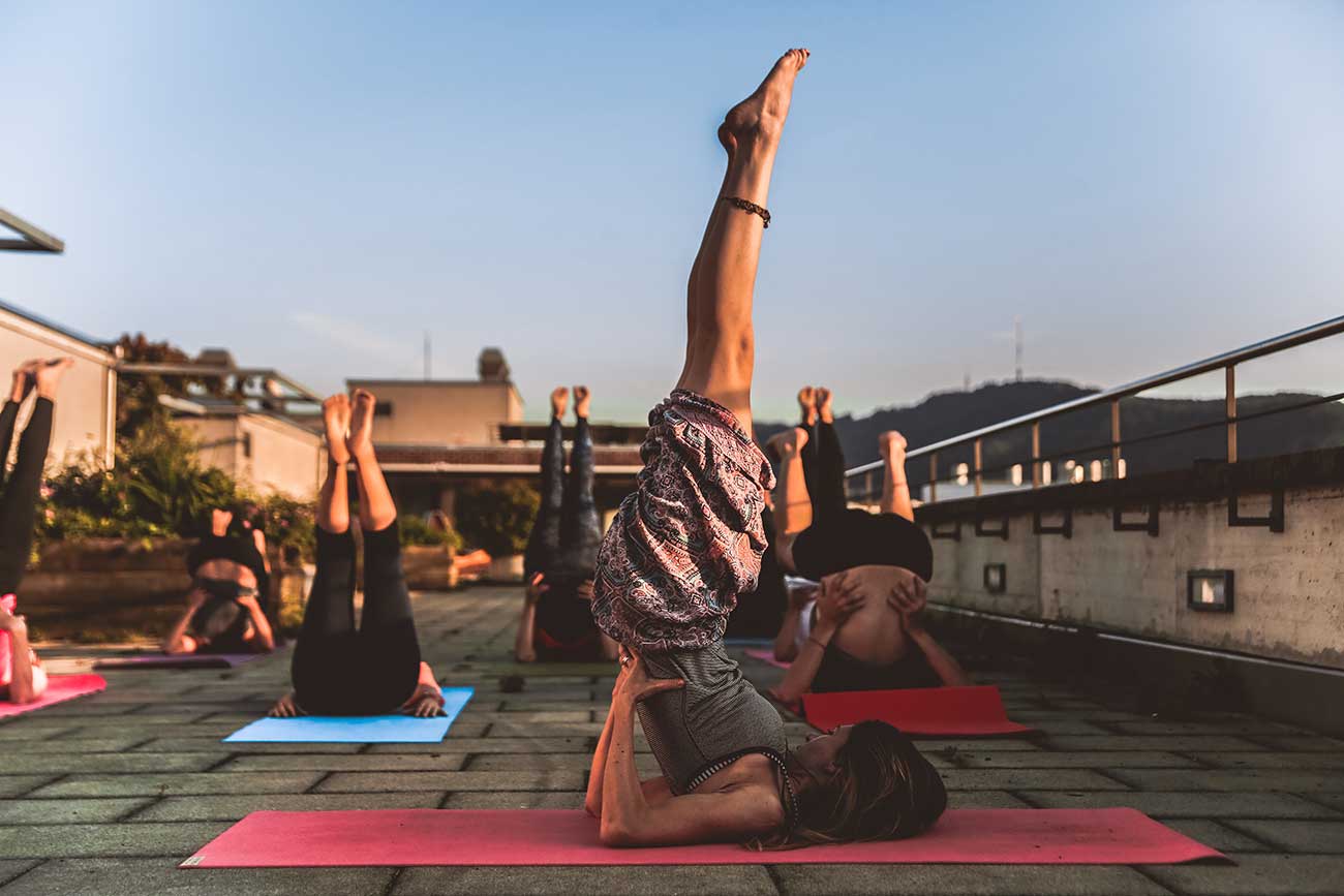 Yoga class on rooftop. Students on their shoulders, with legs raised in the air.
